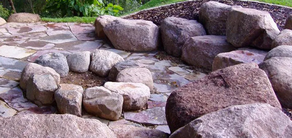 A flagstone patio, boulder scape, and outdoor fire pit designed and built by our team in West Des Moines, IA.