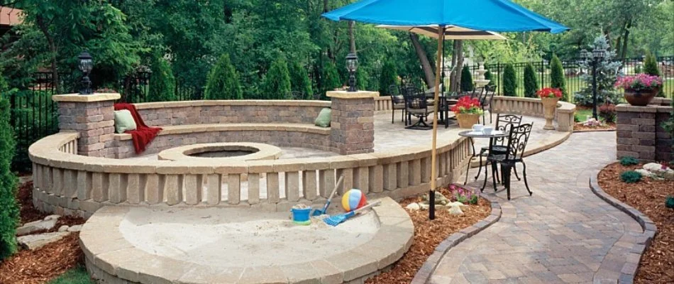 Patio area with a fire pit, seating wall, and sand pit in Bloomfield-Allen, IA.